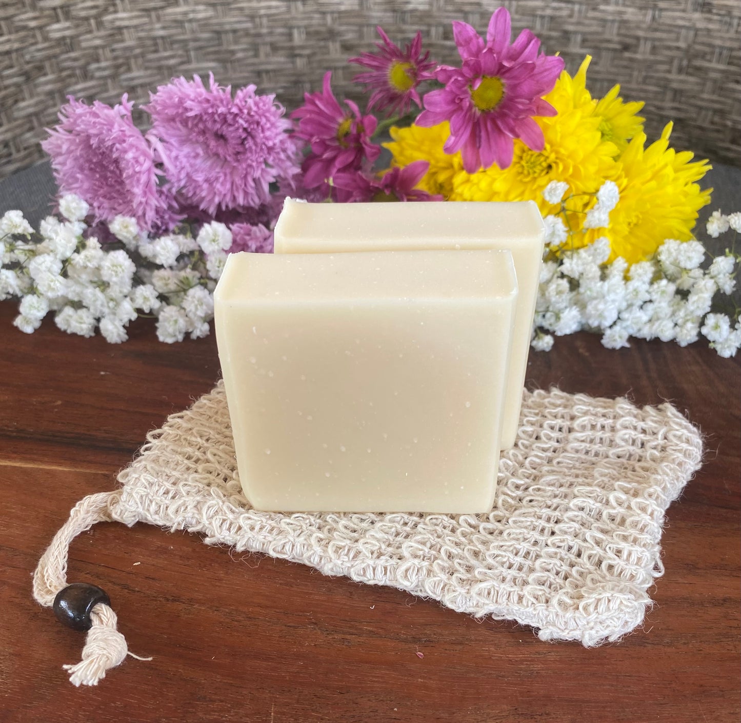 two bars of white soap on top of a woven soap bag with flowers in the background