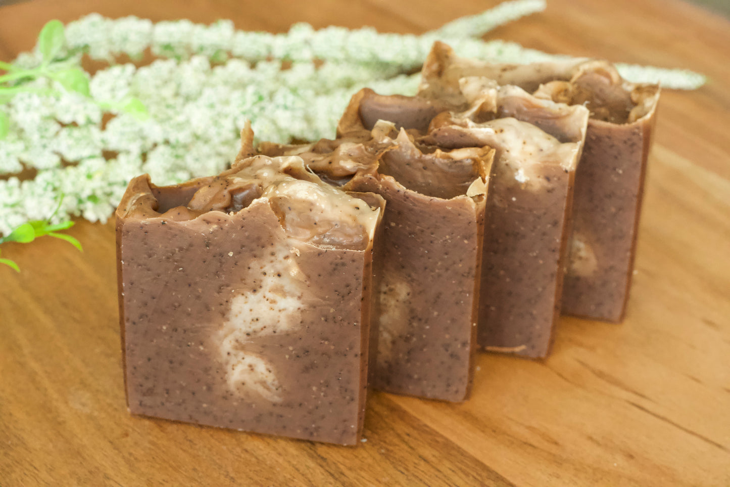 Handmade coffee exfoliating soap bars displayed on a wooden surface with coffee grounds visible on the surface.