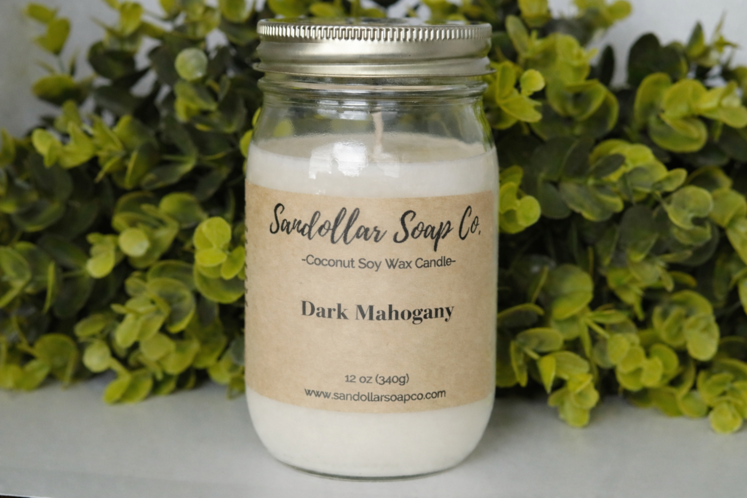 Candle in a mason jar with 'Sandalwood Soap Co.' label against a green leafy background