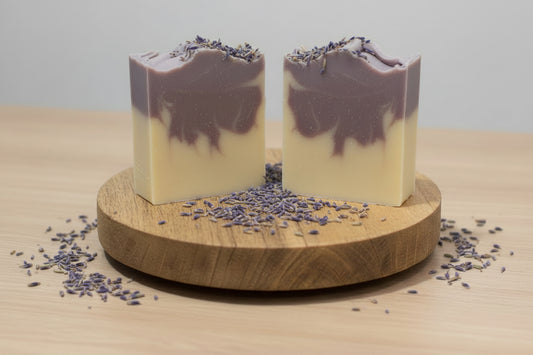 Two bars of lavender soap are being held up over a soap cutter 