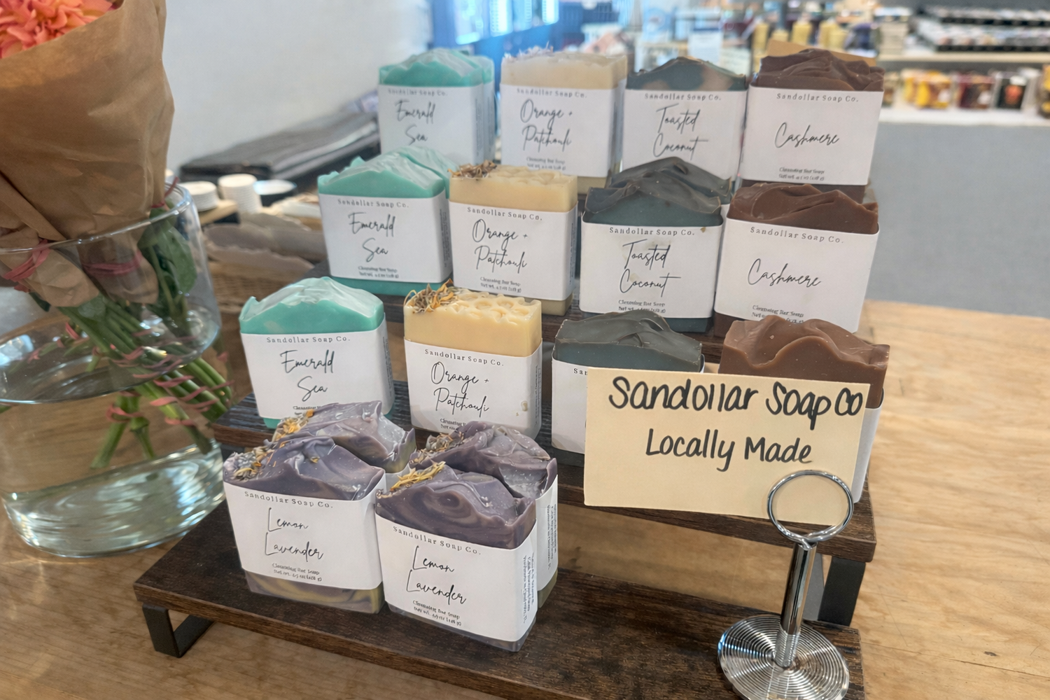 Display of various soaps with a 'Sandollar Soap Co. Locally Made' sign on a wooden stand.