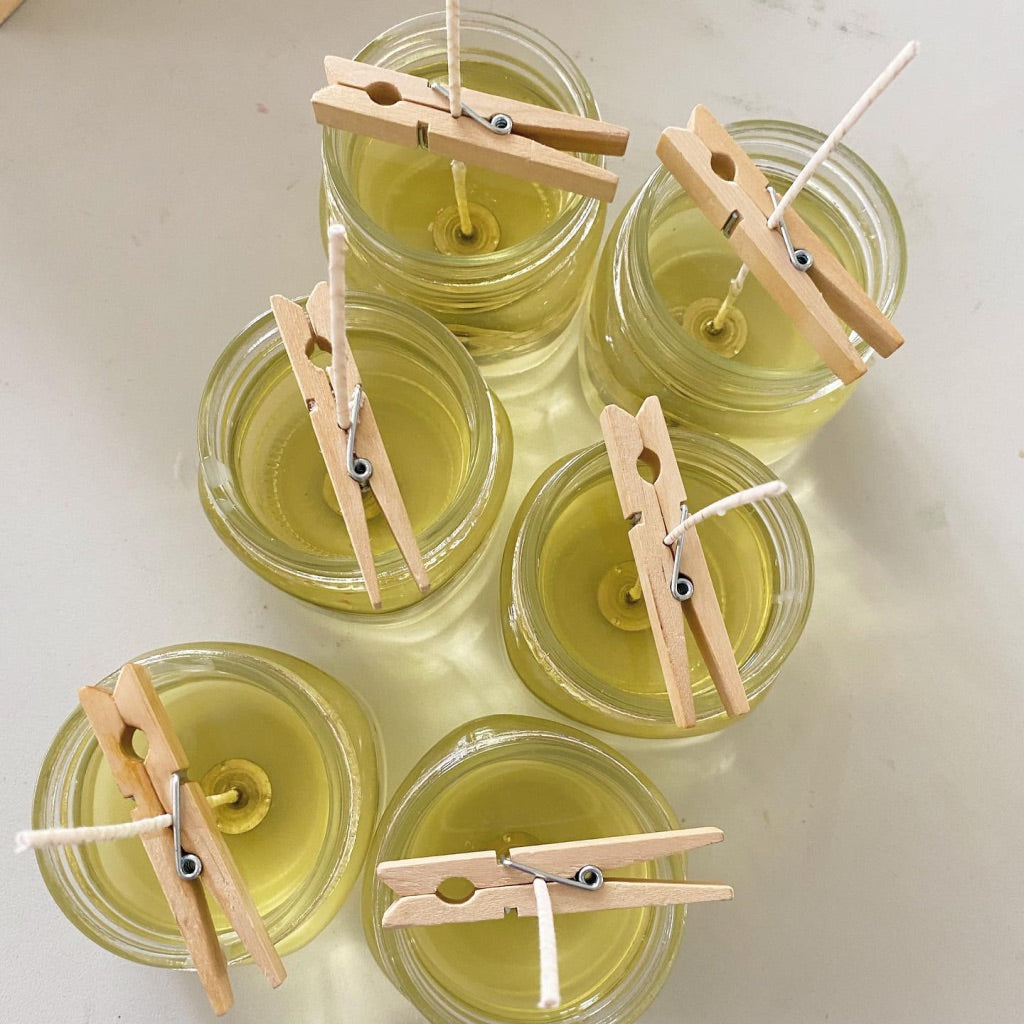 overhead shot of candles that are freshly poured. the Wax has not hardened and there are clothes pins used to center the wick