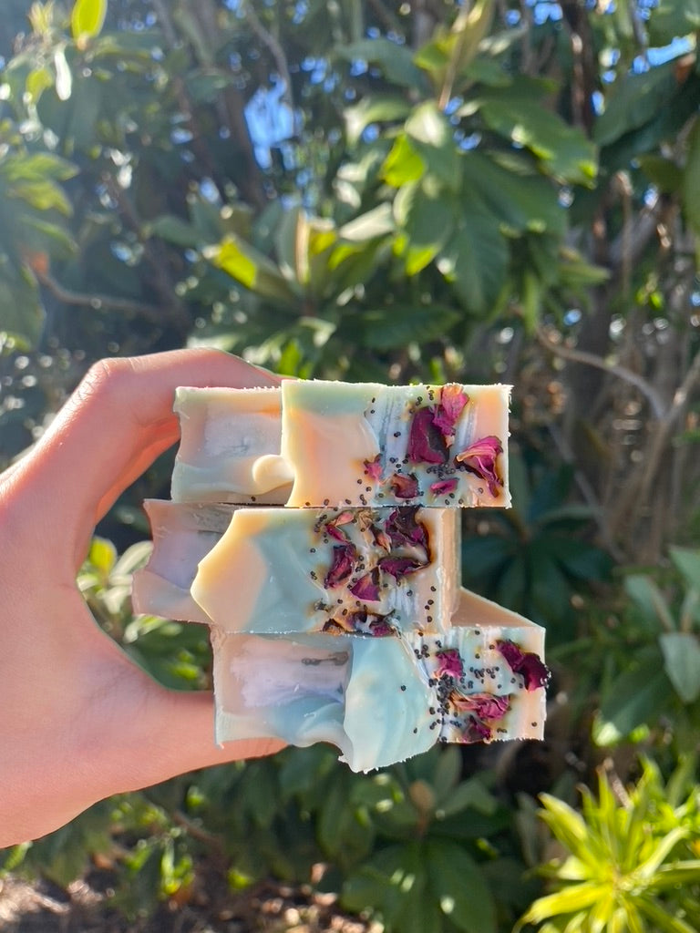 hand holding three bars of soap stacked together in front of a lush background of trees and greenery