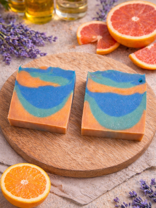 orange, blue, and green bar of soap on a wooden platform surrounded by oils, grapefruits, orange, and lavender