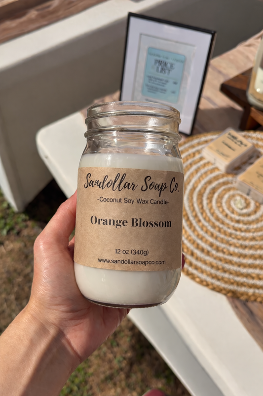 hand holding a mason jar candle labeled "orange blossom" with a blurred background